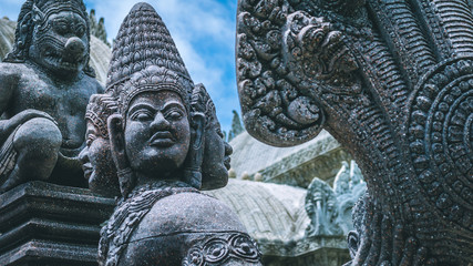 Skulptur of wild people with many bizarre faces. Ancient stone temple in background