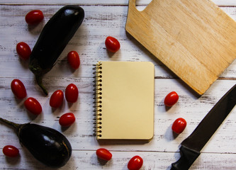 Eggplant, tomatoes, knife and cutting board on a white table