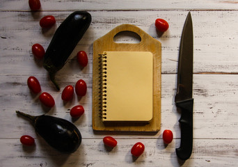 Eggplant, tomatoes, knife and cutting board on a white table