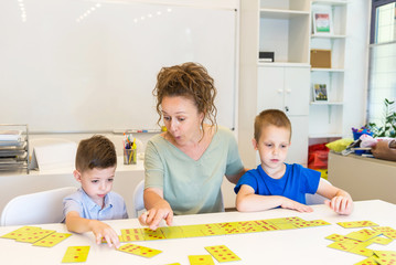 teacher woman play with two child boy domino in classroom