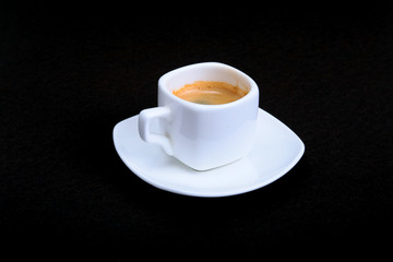 White cup of classic espresso coffee and pralines on black background.