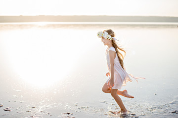 A beautiful girl runs joyfully over the water in a dress at sunset