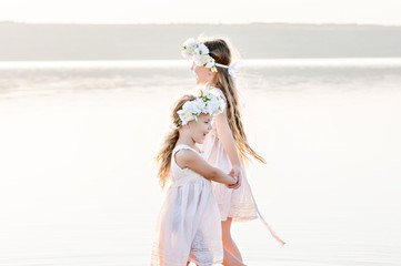 Fototapeta na wymiar Beautiful sisters hold hands and dance on water in dresses and laugh