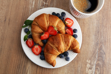 Delicious breakfast with fresh croissants, coffee and ripe berries on old wooden background