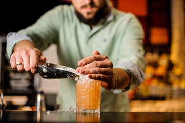 Bartender pours ice into an orange summer cocktail