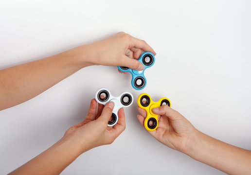 Three hands showing fidget spinners in different colors