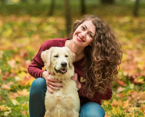 Closeup of curly woman sitting with her dog in autumn leaves outdoors