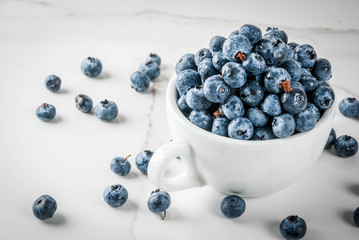 Fresh raw organic farm blueberry in white cup on white marble kitchen background, copy space