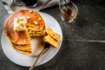 Autumnal traditional food. Stack of pumpkin pancakes with butter, pumpkin seeds and maple syrup. With a cup of coffee. On a black stone table. Copy space