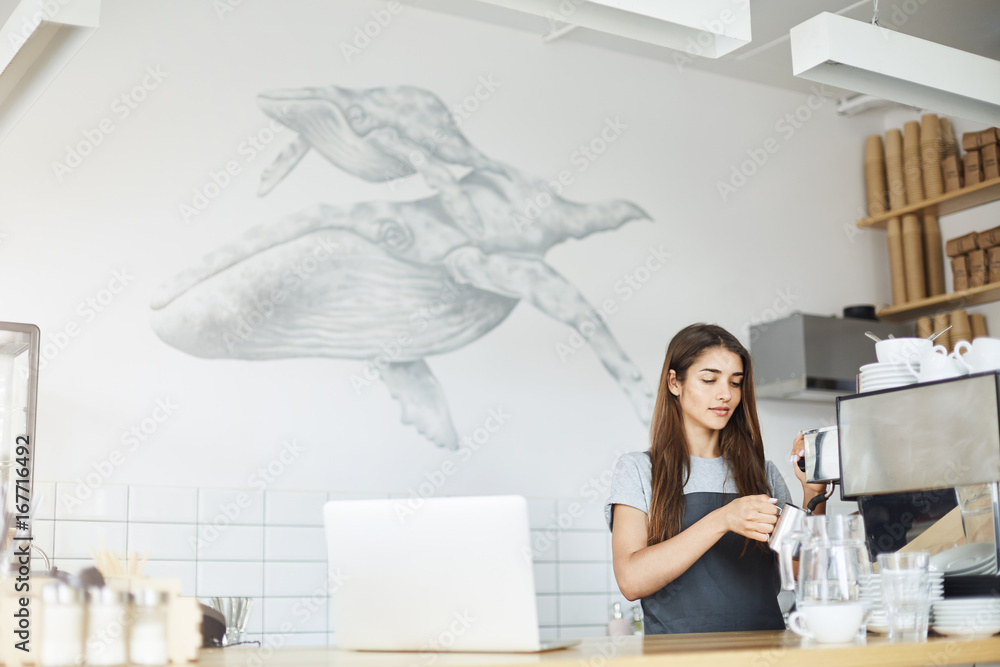 Wall mural Wide shot of barista preparing milk foam on a steamer of espresso machine. Summer job concept.