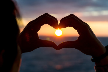 woman shows heart with her hands during sunset