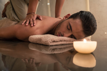 Obraz na płótnie Canvas Young muscular man enjoying the healing benefits of traditional Thai massage at luxury spa and wellness center