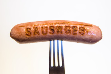 sausage with an inscription pinned on a fork, on a white background.