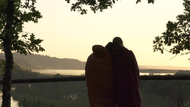 Wide Shot Of Camping Couple In Sleeping Bags Cuddling/Enjoying The Sunset In The Columbia River Gorge, Oregon