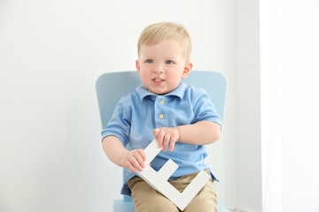 Cute little boy with letter E sitting on chair at home