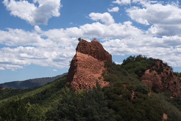 Paisaje de monta&ntilde;as de arcilla roja con vegetaci&oacute;n  y cielo azul despejado con algunas nubes.