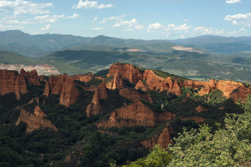 Paisaje de monta&ntilde;as de arcilla roja con vegetaci&oacute;n  y cielo azul despejado con algunas nubes.