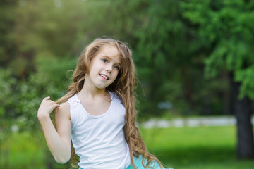 Portrait of beautiful smiling Caucasian little girl with long curly hair against the background of a green park Happy childhood concept
