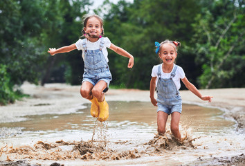 Happy funny sisters twins child girl   jumping on puddles in rubber boots