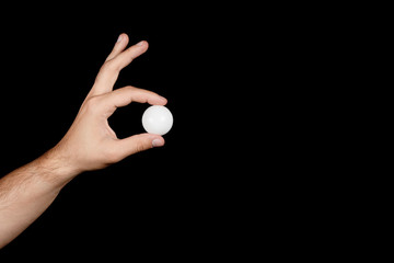 male hand holding between his fingers a ball for ping-pong isolated on black background. the concept of the sport of table tennis - obrazy, fototapety, plakaty
