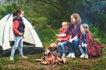 Happy tourist family on journey hike. mother and children fry sausages on bonfire near tent © JenkoAtaman