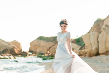 Fototapeta na wymiar Beautiful bride in luxury wedding dress with bouquet at the sea side. Wedding by the sea. Bride walking around the sea near the place of the wedding ceremony.
