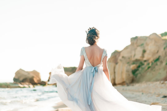 Beautiful bride in luxury wedding dress with bouquet at the sea side. Wedding by the sea. Bride walking around the sea near the place of the wedding ceremony.