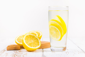 A glass beaker and a jug of cold lemonade on a white wooden background surrounded by lemons.