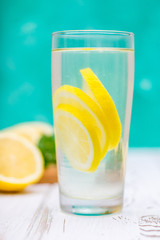 A glass jug with a cold lemonade on a white wooden background surrounded by lemons.