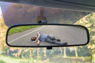 Hit and run concept. View on injured man on road in rear mirror of a car.