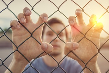 Young man behind wired fence. Immigration concept.