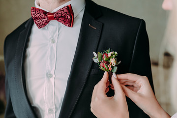 Wedding. Close up bride's hands pinning boutonniere to groom' jacket. Soft focus on boutonniere