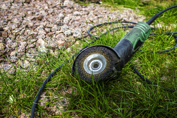Naklejka premium Hand power tool - grinder with a nozzle attachment, top view, on grass and stones, outdoors