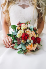 Bride holds a bunch of flowers. Beautiful bridal bouquet with white and peach roses, red peonies, and other flowers. Wedding morning. Close-up.