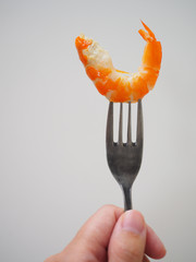 Left hand using stainless steel fork piercing boiled orange shrimp, on white background