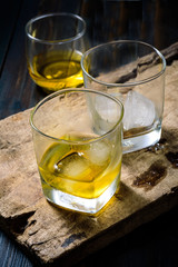 Glass of whiskey with ice placed on wooden planks in vintage style.