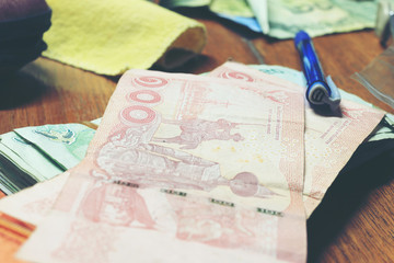 Calculator and money thai banknote with  white notebook paper, pen on wooden table at home office. The concept of financial planning, savings. vintage tone colour and motion blur moving of hand.