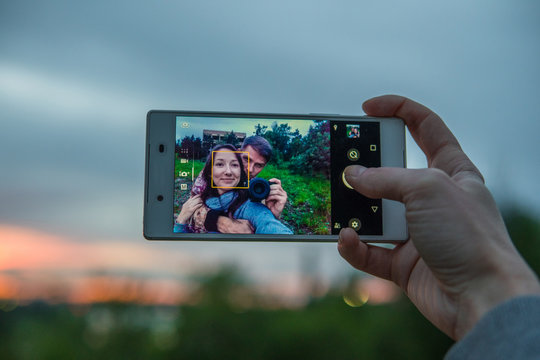 Young loving couple making selfie on phone camera while standing outdoors