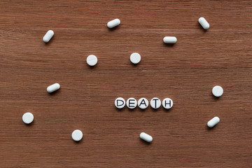 Pills with inscription DEATH on brown wooden surface background