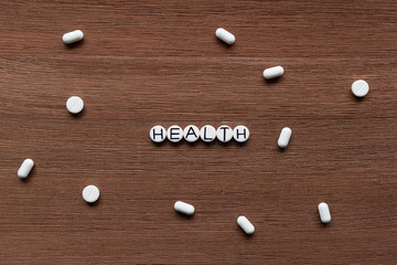White pills with inscription HEALTH on brown wooden surface background