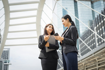 Two business woman standing using smartphone and discussing in front of the office. Business working concept.
