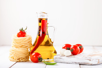 Olive oil with pepper in a bottle, paste, cheese and tomatoes on a light background. Selective focus. Copy space