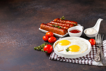 Breakfast - Fried eggs and meat sausages and sauces against a dark background. Selective focus. Copy space
