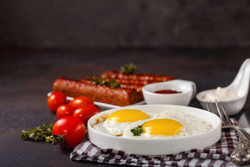 Breakfast - Fried eggs and meat sausages and sauces against a dark background. Selective focus. Copy space