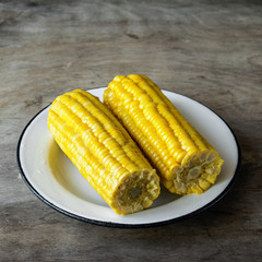 Young corn is served on a white plate on a dark wooden background