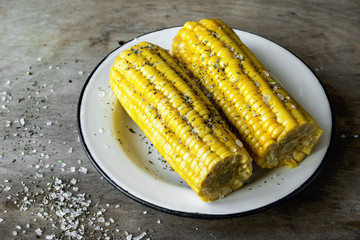 Young corn is served on a white plate on a dark wooden background
