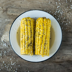 Young boiled corn served on a white plate on a dark wooden background