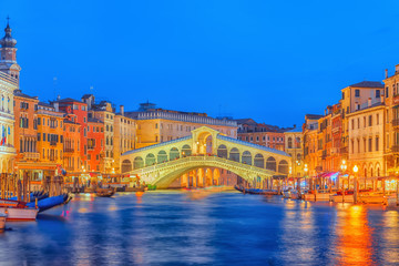 Fototapeta na wymiar Rialto Bridge (Ponte di Rialto) or Bridge of Sighs and view of the most beautiful canal of Venice - Grand Canal and boats, gondolas, mansions along. Night view. Italy.