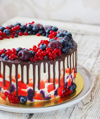 Bright festive cake with berries and chocolate on a white wooden background