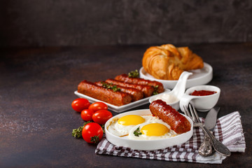 Breakfast - Fried eggs and meat sausages and sauces against a dark background. Selective focus. Copy space